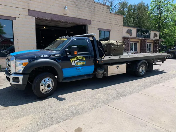 Precision Towing rollback with a pickup in front of the Evart shop