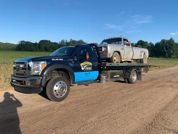 Rollback carrying a classic pickup on a gravel lot