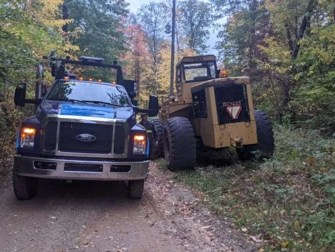 Service truck on a wooded two-track beside a disabled loader